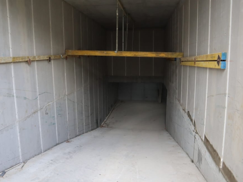 Concrete wall systems forming a narrow underground corridor with temporary timber bracing and smooth precast panels.