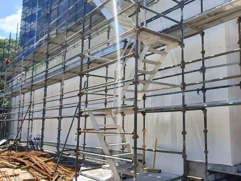 Scaffolding erected around tall insulated wall panels on a building site, ready for concrete block fill installation.