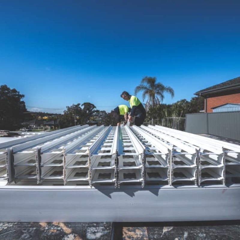 orkers installing permanent formwork panels aligned in rows on construction site under clear blue sky