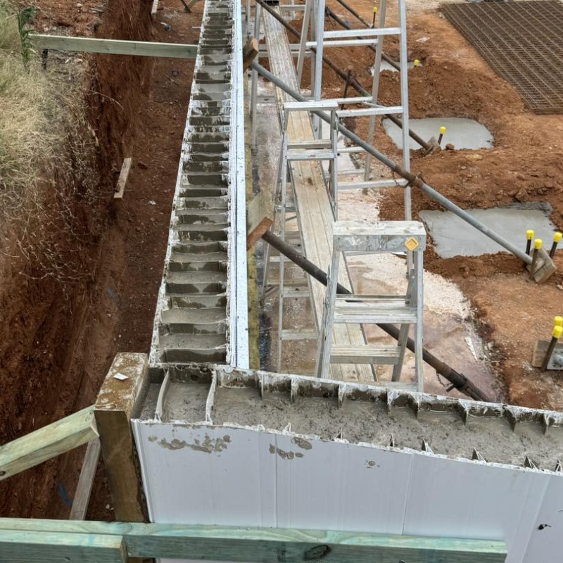 Concrete wall pour using formwork systems with scaffolding and reinforced concrete foundation trench on active construction site.