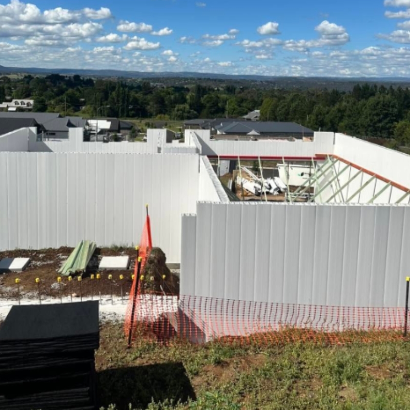 A construction site featuring extensive white panel wall formwork systems, ready for concrete pouring, under a partly cloudy sky.