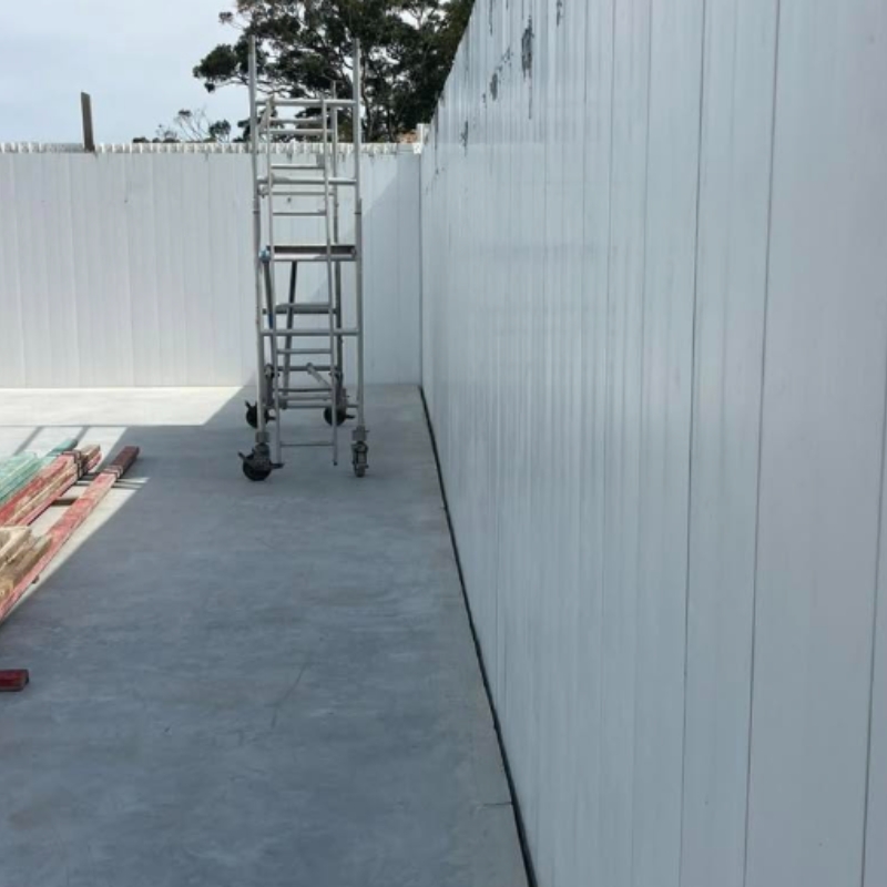 A concrete slab floor alongside tall, vertical white composite panels assembled into a rigid wall formwork design.
