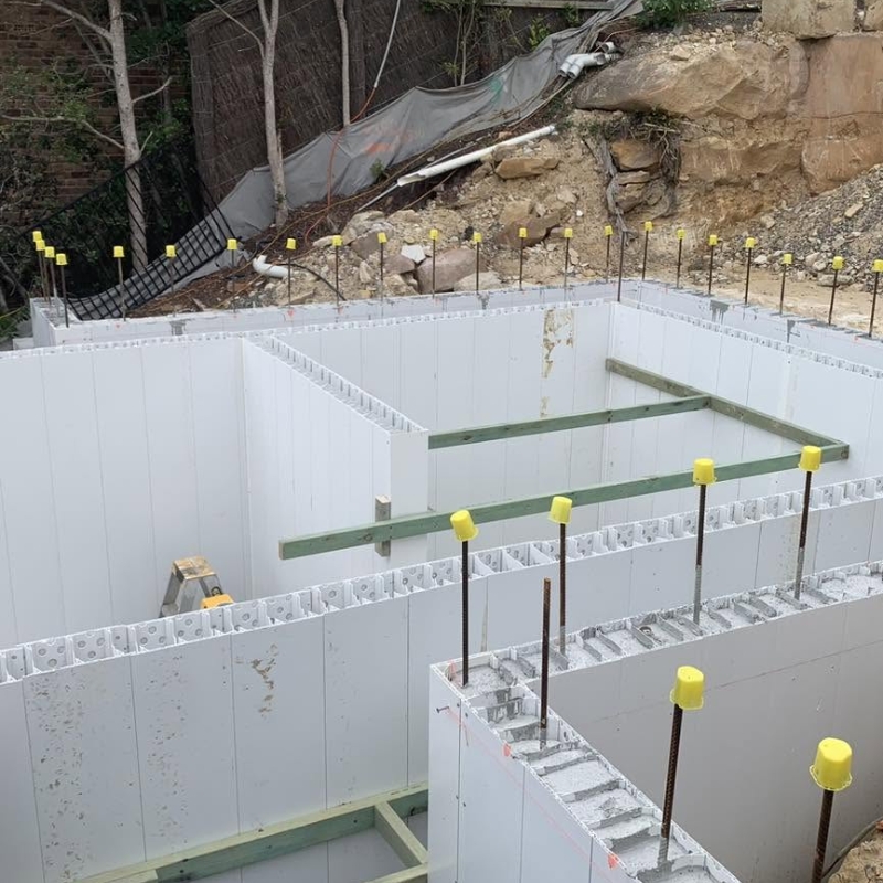 A permanent modular formwork design with white PVC panels and vertical steel rebar featuring yellow safety caps.