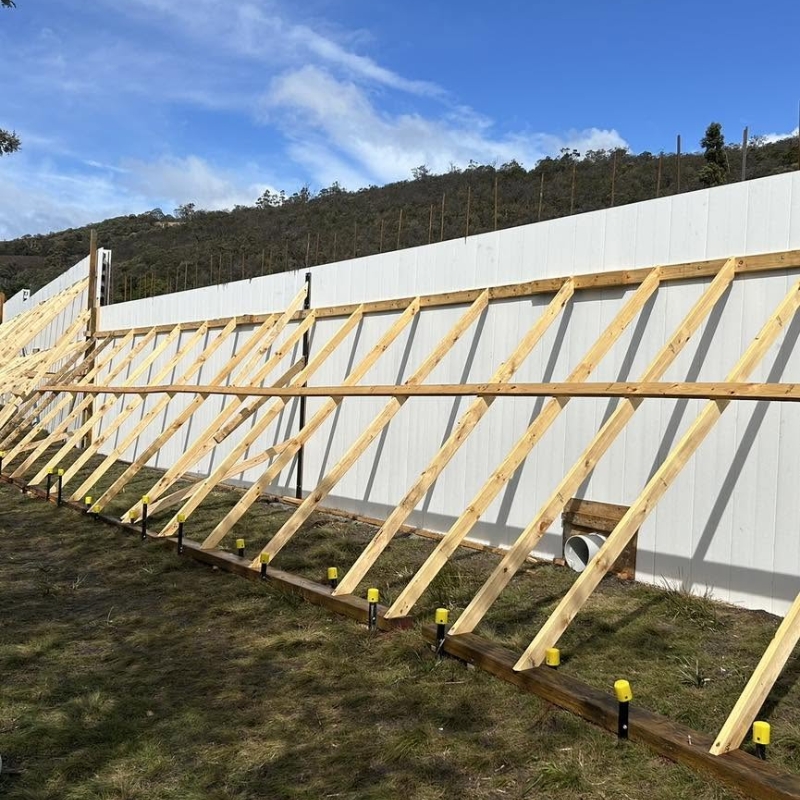 A long white permanent formwork systems wall supported by a row of diagonal timber bracing struts outdoors
