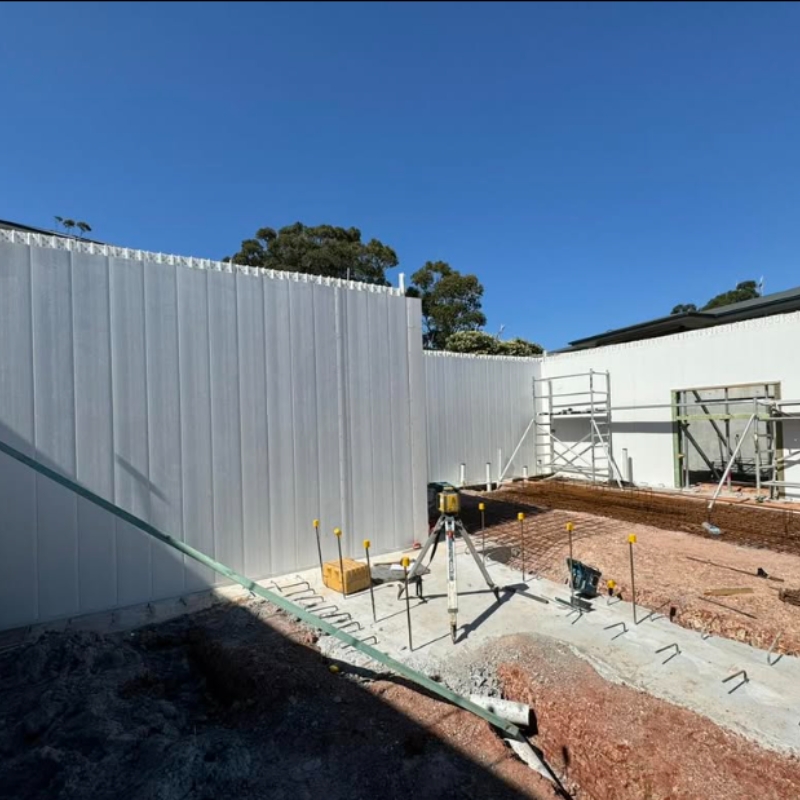 Tall white PVC formwork panels assembled to construct permanent basement walls on a sunny construction site.