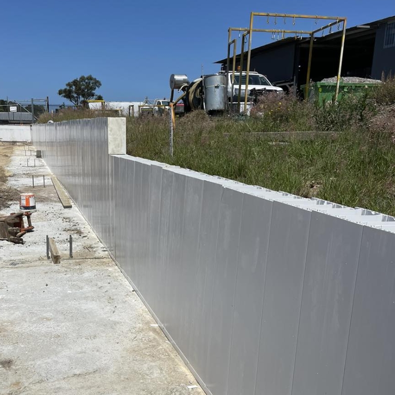 Smooth light-grey PVC forms installed to build durable concrete retaining walls along a outdoor sloping boundary.
