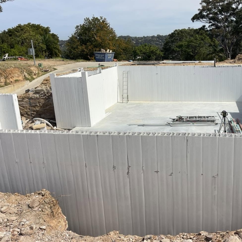 White permanent PVC formwork system panels installed for a building basement foundation on an outdoor construction site.